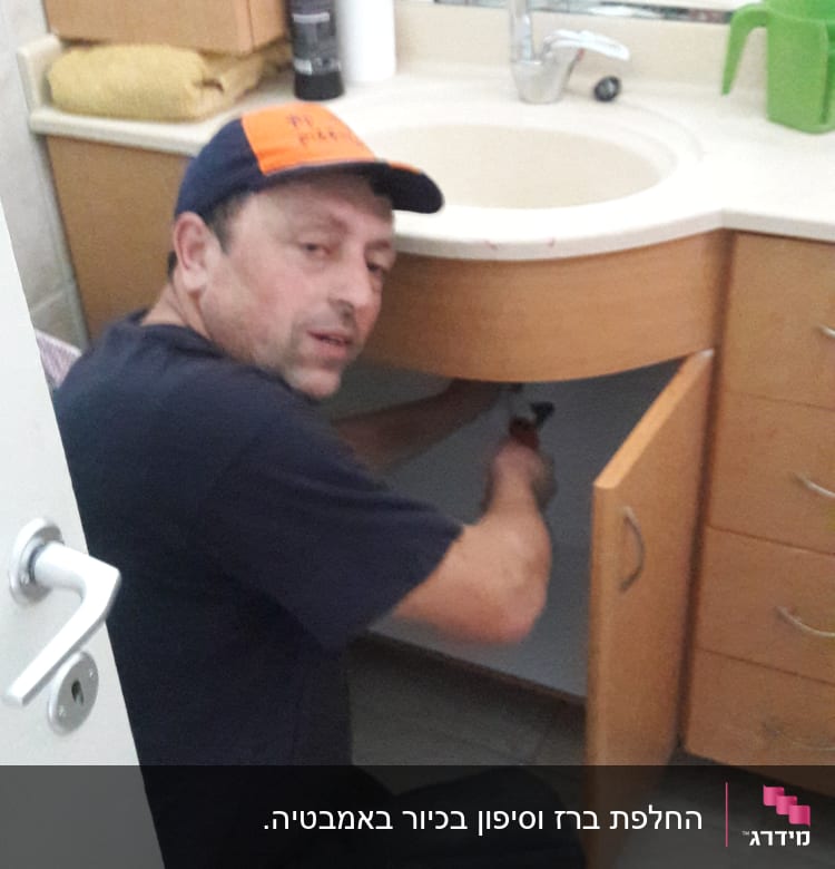 אדם מתקן צנרת מתחת לכיור בחדר אמבטיה